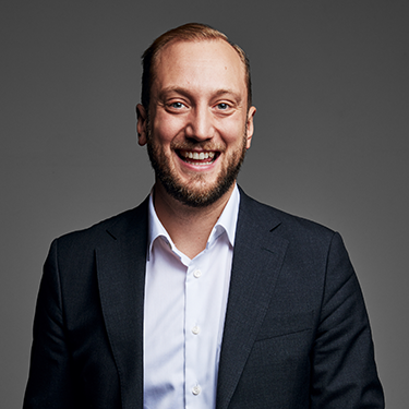 Christofer Laurell smiling in a suit infront of a grey background