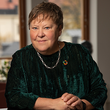 Ingrid Petersson sitting in front of a window wearing a green shirt and a Global Goals pin.