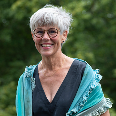 Susanne Ekstedt is smiling & standing outside in a blue and black shirt.