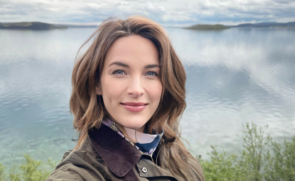 Kajsa Li Paludan standing in front of a lake with clouds reflected in it.