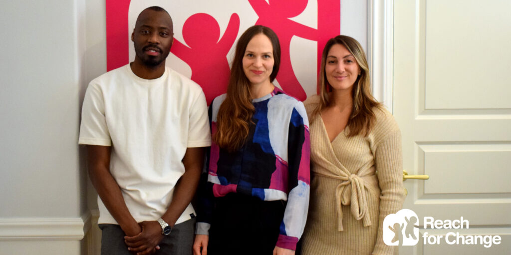 Three people looking at the camera and Reach for Change logo in the right bottom corner.