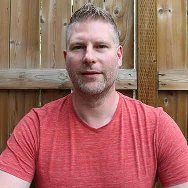 Marek Hejduk wearing a red shirt in front of a wooden fence