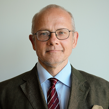 Andreas Umland in a suit in front of a grey background (semi closeup)