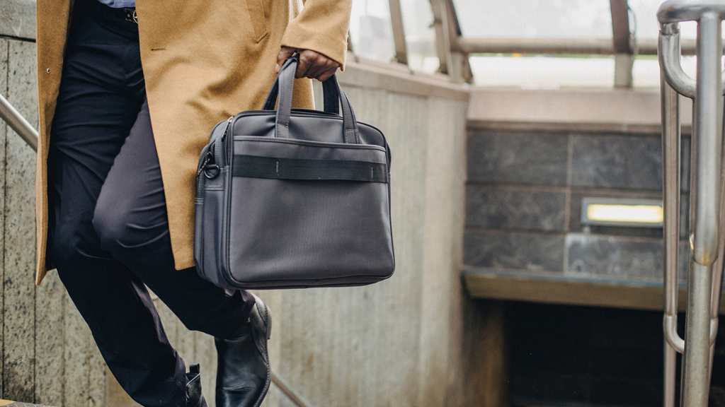 Bottom half of a man walking up from a subway station with a briefcase